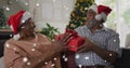 Image of snow falling over senior african american couple wearing santa hats Royalty Free Stock Photo