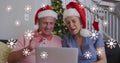 Image of snowflakes over senior caucasian couple wearing santa hats and using tablet Royalty Free Stock Photo