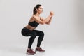 Image of sporty athletic woman in sneakers and tracksuit squatting doing sit-ups in gym, isolated over gray background Royalty Free Stock Photo