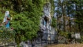 Image of a statue of Bernadette praying to Our Lady of Lourdes in a natural grotto