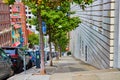 Steep hill with cars parked beside sidewalk with green trees evenly spaced down path in city