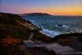 Steps going down hill toward blue ocean with sunset sky and distant city above cliff Royalty Free Stock Photo