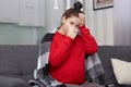 Image of stressful sad pregnant woman has terrible headache, fever and running nose, suffers from constant sneezing, sits at sofa