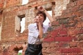 Image of a stylish beautiful woman in a white shirt and leather skirt in a park against the background of a destroyed building.