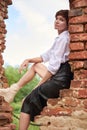 Image of a stylish beautiful woman in a white shirt and leather skirt in a park against the background of a destroyed building.