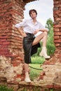 Image of a stylish beautiful woman in a white shirt and leather skirt in a park against the background of a destroyed building.