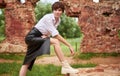 Image of a stylish beautiful woman in a white shirt and leather skirt in a park against the background of a destroyed building.