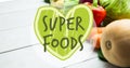 Image of superfoods text in green on green heart, over fresh vegetables on white boards