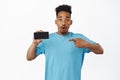 Image of surprised african american man gasp say wow, pointing finger at mobile phone screen with amazed face, showing Royalty Free Stock Photo