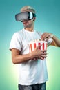 Image of surprised bearded hipster man wearing virtual reality goggles eating popcorn from bucket in neon lights.
