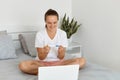 Image of surprised happy young woman holding pregnancy test while sitting in front of laptop on bed, female looking for Royalty Free Stock Photo