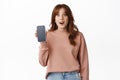 Image of surprised teenage girl drop jaw, showing advertisement on smartphone screen, recommend app on phone, standing Royalty Free Stock Photo