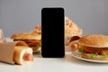 Image of table with different fast food and smart phone with balck blank screen, copy space for advertisement of fast food