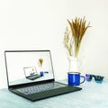 Image of a thin laptop next to a cup of coffee, a decorative metal jug and sunglasses