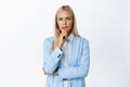 Image of thoughtful blond corporate woman, looking at camera with serious face, thinking, listening to you, standing in Royalty Free Stock Photo