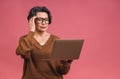 Image of tired depressed mature aged senior business woman standing isolated over pink background using laptop computer. Portrait Royalty Free Stock Photo