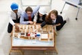 Image is topview. A man African American engineering and caucasian holds coffee. In group meetings Viewing a model building model