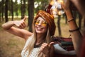Image of trendy hipster woman, wearing stylish accessories smiling and showing peace sign while resting in forest camp Royalty Free Stock Photo