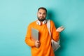 Image of troubled young man with headphones and backpack, shrugging confused and holding laptop, standing over light Royalty Free Stock Photo