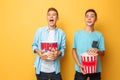 Image of two excited beautiful teenagers, guys watching an interesting movie and eating popcorn on a yellow background