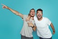 Portrait of two happy young men pointing fingers away isolated over light blue background. Friendship concept Royalty Free Stock Photo