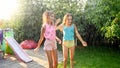 Image of two happy laughing teenage girls jumping and dancing under warm summer rain at house backyard garden. Family Royalty Free Stock Photo