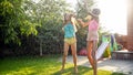 Image of two happy laughing teenage girls jumping and dancing under warm summer rain at house backyard garden. Family Royalty Free Stock Photo