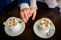 Image of two people's hands with wedding rings. Coffee or hot chocolate cups on wooden table in a cafe. Royalty Free Stock Photo