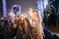 Image of two women with Bengal lights on winter walk on background of decorated spruce