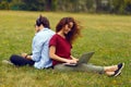 Image of a two young person, sitting behind, using laptop and listening music in headphone, on a grass in open air. Royalty Free Stock Photo