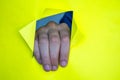 Image of unrecognizable man gesturing through torn paper wall yellow background. Body language concept. The hole in the wall. Like Royalty Free Stock Photo