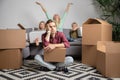 Image of upset man sitting on floor and women with boy and girl sitting on gray sofa among cardboard boxes Royalty Free Stock Photo