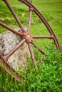 Vertical shot of rusty wheel resting against textured concrete block fragment in grassy field