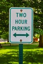 Vertical of tall green Two Hour Parking sign with green lawn and trees in background