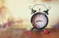 Image of vintage alarm clock next to autumn leaves on wooden table in front of abstract blurred background. retro filtered Royalty Free Stock Photo