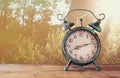 Image of vintage alarm clock on wooden table in front of rustic country side landscape background. retro filtered Royalty Free Stock Photo