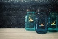 Image of vintage decorative magical mason jars with candle light on wooden table. Glitter overlay Royalty Free Stock Photo