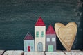 Image of vintage wooden colorful houses and fabric heart on wooden table in front of blackboard