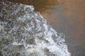 SURGING WHITE FROTH SPILLING INTO WATER WITH AMBER COLOURED BOTTOM