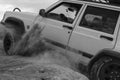 Image of a white jeep trying to move in the soil in black and white.