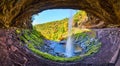 Wide angle in cave space behind waterfall over cliff edge with fall forest mountains behind Royalty Free Stock Photo