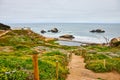 Wide view of sandy trail with stairs leading down to ocean with abandoned structure and beach