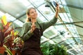 Image of woman gardener wearing apron taking selfie photo with plants while working in greenhouse