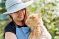 Image of woman in hat holding ginger cat in garden Royalty Free Stock Photo