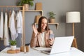 Image of woman in jacket working on laptop in home office against clothes hang on shelf, having break, making video call with Royalty Free Stock Photo