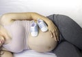 Image of A woman pregnant reclining on bed and touching or caressing her belly with baby shoes. Royalty Free Stock Photo