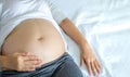 Image of A woman pregnant reclining on bed and touching or caressing her belly with hands. Royalty Free Stock Photo