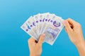 Image woman`s hands which holds British pounds in her hands isolated over blue studio background