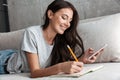 Image of woman writing in diary book and holding smartphone on sofa at home Royalty Free Stock Photo