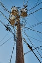Wooden telephone pole with three barrels on top and lots of converging phone lines on a clear blue sky